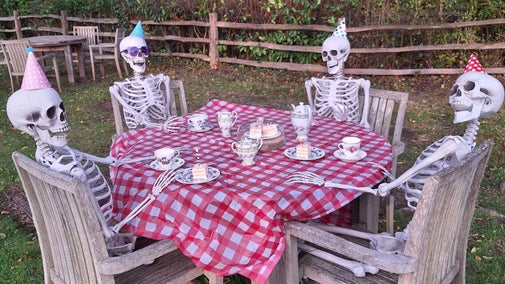 Four skeletons in party hats having afternoon tea around a table